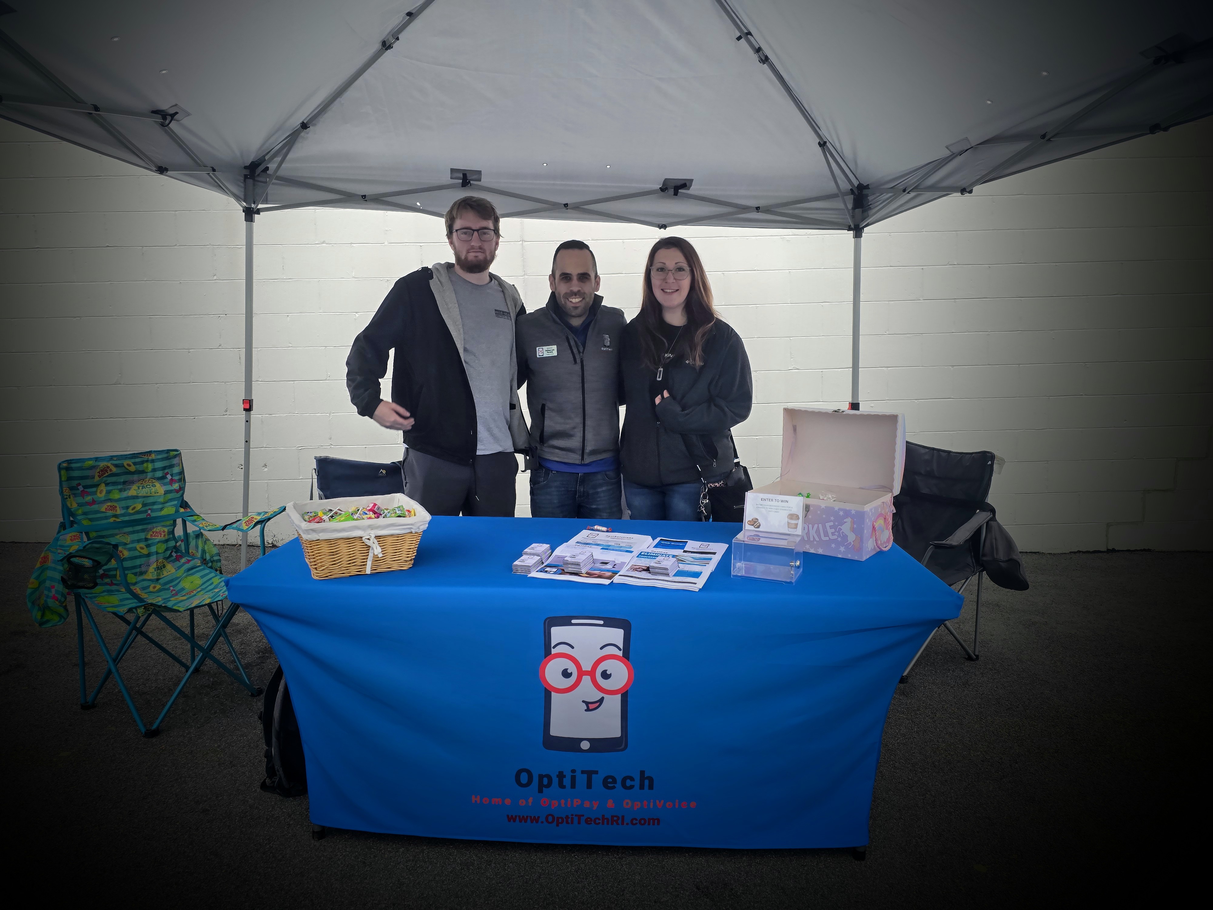 OptiSolutions team members at a community outreach event with branded table and promotional materials